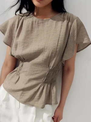 Beige blus med smockdetaljer - Säljer en beige blus med korta, fladdriga ärmar och smockdetaljer i midjan som ger en snygg siluett. Tillverkad i ett lätt, strukturerat bomullstyg som känns luftigt och skönt. Perfekt till både jeans och kjol för en avslappnad look. Passar S och M