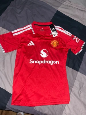 Manchester United 26/27 hemmatröja - Manchester United hemmatröja till kommande säsong 2026/2027, köpt från adidas, lapp och påse finns kvar. Säljer då den inte passade mig. Helt ny endast provad. Matheus cunha på ryggen.
