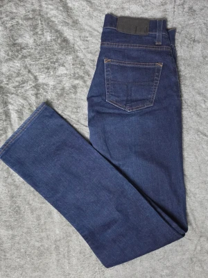 Tiger of Sweden Jeans Skogsberg Severe blå W29/L32 - Mörkblå jeans från Tiger of Sweden Jeans, modell Skogsberg med tvätt/program Severe. Klassisk femficksmodell med orange kontrastsömmar och lätt stretch i materialet. Stilren mörk denim som fungerar både till vardags och mer uppklätt.  Storlek W29/L32  Mycket fint begagnat skick med endast lättare tecken på användning.  Mått Midja: ca 38 cm Grenhöjd: ca 21 cm Ytterbenslängd: ca 99 cm Innerbenslängd: ca 77 cm Benöppning: ca 17 cm  Material 98% bomull 2% lycra