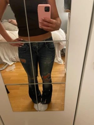 Mörkblå bootcut jeans med slitningar - Säljer ett par mörkblå bootcut jeans med coola slitningar och hål på både fram- och baksida. Jeansen har låg midja och klassiska fickor. Jag har själv sytt ut dem till Botcutt 
