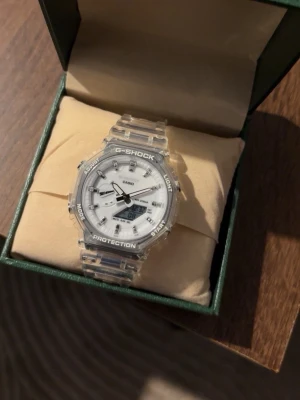 Klocka - Säljer en klocka med transparent armband och vit urtavla. Klockan har digital display, tydliga markeringar och robust design. Perfekt för dig som gillar en modern och sportig stil.