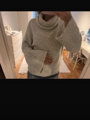 Ljusgrå stickad polotröja med vida ärmar - Mysig stickad polotröja med oversized passform och vida ärmar. Tröjan har en hög, rullad polokrage och är tillverkad i ett fluffigt, mjukt material som känns extra skönt mot huden. Perfekt för kyliga dagar.
