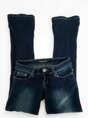 Mörkblå bootcut jeans Goodies - Snygga mörkblå bootcut jeans från Goodies med klassisk femficksmodell och slitningar framtill. Jeansen har en markerad midja, silverfärgade knappar och detaljer samt logga bak på linningen. Perfekta för en trendig och avslappnad look.