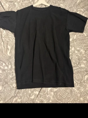 Svart basic t-shirt i bomull - En enkel svart t-shirt med rund hals och korta ärmar. Tillverkad i mjuk bomull och har en klassisk passform som funkar till det mesta. Perfekt att matcha med jeans eller shorts för en clean look.