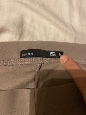 Beige utsvängda leggings från 157 - Säljer ett par beige leggings från 157 i storlek M. De har en utsvängd passform nedtill och är tillverkade i ett stretchigt material som sitter skönt på kroppen. Perfekta för dig som gillar en enkel men trendig look.