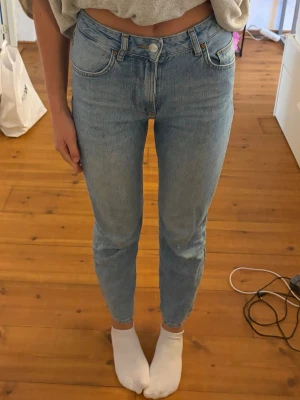 Ljusblå raka jeans med hög midja - Säljer ett par ljusblå jeans med rak passform och hög midja. Klassisk femficksmodell med knapp och dragkedja framtill. Jeansen har en tidlös tvätt och är perfekta till vardagslooken. Materialet är denim i bomull.