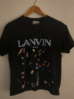 Lanvin x gallerey dept. T-shirt - Snygg svart t-shirt från Lanvin och gallerey dept. med stort tryck framtill och färgstänk i olika nyanser. Klassisk passform och rund halsringning. Perfekt för dig som vill ha en unik och trendig look.
