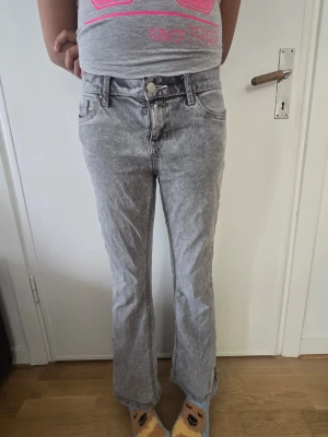Grå bootcut jeans med tvättad look - Säljer ett par grå bootcut jeans med snyggt tvättad effekt. Jeansen har hög midja, klassiska fem fickor och utsvängda ben. Perfekta för dig som gillar en avslappnad men trendig stil. Materialet känns mjukt och följsamt.