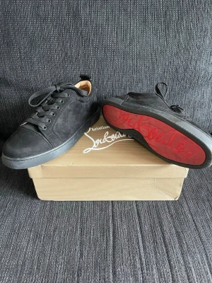 Svarta Christian Louboutin sneakers - Snygga svarta sneakers från Christian Louboutin i mocka med klassisk röd sula och svarta skosnören. Låg modell med diskret logga på sidan och detaljer i svart. Kommer med originalkartong, dustbag och certifikat.