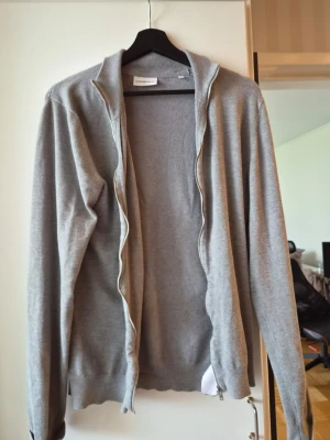 Grå ziptröja i bomullsblandning - Snygg grå ziptröja med lång ärm och hög krage. Tillverkad i mjuk bomullsblandning, perfekt att slänga på sig över en t-shirt. Enkel och stilren design utan tryck eller mönster.