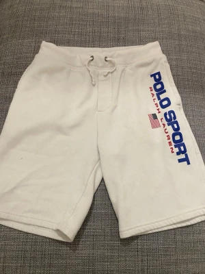 Vita shorts från Polo Sport - Snygga vita shorts från Polo Sport Ralph Lauren med blå och röd logga längs benet. De har snörning i midjan och en bakficka. Perfekta för sommaren och riktigt sköna tack vare mjukt bomullsmaterial.