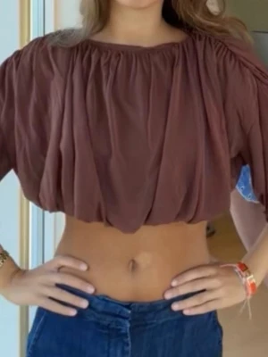 Brun croppad blus med ballongärm - Säljer en brun croppad blus med vida ballongärmar och rynkade detaljer. Toppen har en lös passform och är gjord i ett tunt, luftigt tyg som ger en avslappnad look. Perfekt till höga jeans eller kjol för en trendig stil.