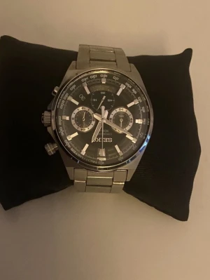 Seiko silverfärgad kronografklocka - Stilren Seiko kronografklocka i silverfärgat rostfritt stål med svart urtavla och tydliga indexmarkeringar. Klockan har flera små urtavlor för tidtagning och datum, samt robust länkarmband. Perfekt accessoar för dig som gillar klassisk och sportig stil.
