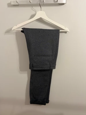 grå kostymbyxor - Snygga mörkgrå kostymbyxor med klassisk passform och uppvikta benslut. Byxorna har diskreta bakfickor och är perfekta för en stilren look. Storlek Xl men passar bättre till L eftersom den är liten i storlek! 