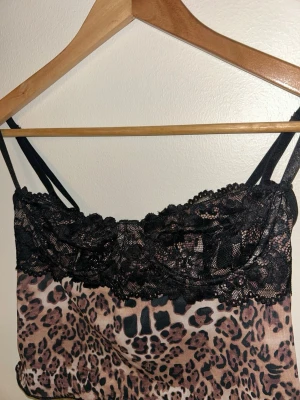 Leopardmönstrad spetsbody med smala band - Snygg leopardmönstrad body med svarta spetsdetaljer över bysten och tunna axelband. Justerbar knäppning bak och mjukt, stretchigt material. Perfekt för dig som vill ha något extra till underkläderna. Djurmönster och spets ger en trendig look.