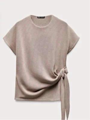 Beige topp med knyt i sidan - Säljer en stilren beige topp med korta ärmar och rund halsringning. Toppen har en snygg knyt-detalj i sidan som ger en unik touch. Perfekt att matcha med både jeans och kjol för en trendig look.