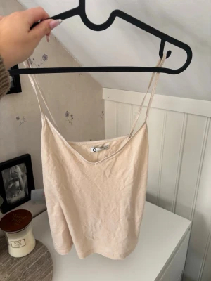Beige linnetopp med tunna axelband - Säljer en enkel och stilren beige linnetopp med tunna axelband. Toppen har en rak passform och är perfekt för varma dagar. Materialet känns mjukt och lätt mot huden. Passar till det mesta och är ett måste i garderoben. Skulle säga att den passar xs också. 