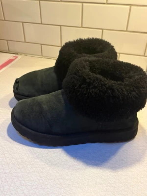 Svarta uggs - Ett par svarta uggs med mjuk och fluffig fårskinnskant. Utsidan är i mocka och sulan är tjock och stabil. Den har ett skraphål på framsidan som går att laga hos en skomakare. Perfekta för att hålla fötterna varma inomhus eller utomhus. 