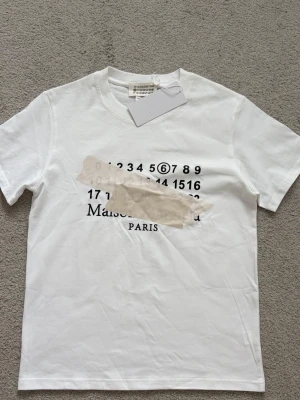 Vit Maison Margiela t-shirt - Snygg margiela T-shirt med snygg tryck på framsidan. Storleken är M men sitter som S. Priset går att diskutera.