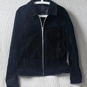 Svart mockajacka Rockandblue - Snygg svart mockajacka från Rockandblue med klassisk krage och silverfärgad dragkedja framtill. Jackan har raka ärmar och två sidofickor. Perfekt för dig som vill ha en stilren och tidlös look.