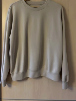 Beige sweatshirt från 157, storlek S - En stilren beige sweatshirt från 157 i storlek S. Tröjan har rund halsringning, långa ärmar och ribbade muddar vid ärmslut och nederkant. Tillverkad i mjukt material som passar perfekt till en avslappnad look.