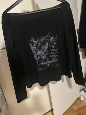 Svart långärmad topp med tryck - Svart långärmad topp med bred urringning och tryck framtill i lila toner. Trycket har texten Fallen Angel. 