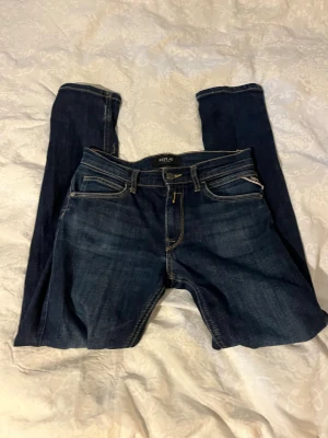 Mörkblå slim fit jeans från Replay - Snygga mörkblå slim fit jeans från Replay med klassisk femficksmodell och kontrastsömmar. Jeansen har en något tvättad look och är tillverkade i ett mjukt denimtyg som sitter skönt. Perfekta för dig som gillar en stilren och modern look. Replay labeln har lossnat som ni ser på bild 3