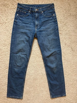 Blå raka jeans med fem fickor i nyskick - Endast använda 2-3 gånger, så fortfarande nyskick. Klassiska blå jeans i rak modell med fem fickor och normalhög midja. Jeansen har tydliga sömmar och metallknapp i midjan. Materialet är denim i bomull och passformen är avslappnad men ändå snyggt figurnära.