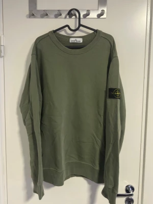 Stone Island sweatshirt  - Säljer en stilren grön sweatshirt från Stone Island med klassisk rund hals och den ikoniska loggan på vänster ärm. Passar som L,  Tröjan har en relaxed fit och är tillverkad i mjuk bomull. Perfekt för en casual look. Snabb Affär=Bra pris👍