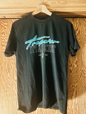 Svart t-shirt med tryck - Trap Star  'It's a secret' och grafiskt tryck i turkos och vitt på bröstet. Rund halsringning och korta ärmar. Perfekt för dig som gillar streetwear och vill sticka ut lite extra.