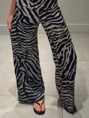 Vida byxor med zebramönster - Snygga vida byxor med zebramönster i svart och beige. Byxorna har hög midja och raka, lösa ben för en avslappnad look. Tillverkade i ett mjukt och följsamt material som känns skönt mot huden. Perfekta för dig som vill sticka ut med ett djurinspirerat print.