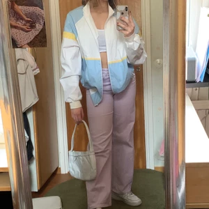 Luftig Jacka - Söt ”windbreaker” liknande jacka i pastell blått och gult. Har ICA loggan väldigt litet på ena sidan syns knappt. Strlk M men är oversized.