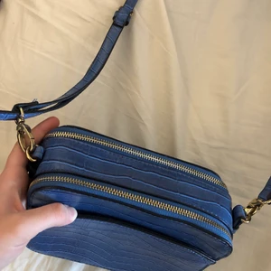 Liten blå väska - En liten blå väska med guldiga detaljer som är i nästintill nyskick, går även att justera längden på bandet💓