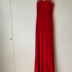 Vacker röd långklänning - Vacker röd långklänning. Osäker på märket. Fantastisk rygg med låg skärning och dekorativa detaljer i guld och glittriga stenar. Supersmickrande modell och mjukt och stretchigt material. Storlek S. Material enligt bild. Helt oanvänd och i jättefint skick utan anmärkningar.