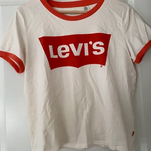 Vit Levis tröja - En vit Levis tröja med orangea detaljer. Begagnat skick. Frakten är inte inkluderad i priset då jag inte vet helt 100 vad den blir. Köparen står för frakt.  Allt som säljs kommer från ett rent djur- och rökfritt hem.