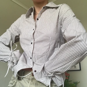 Brunrandig skjorta med knytning från KAFFE - Supersnygg skjorta med knytning runt handlederna! Ser svartvit ut på bilderna men ränderna är bruna🤎