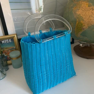 Blå liten väska - Jättegullig blå korgväska med dragsko som stängning, går också ha den osynlig om man vill ha det öppet. Finns någon enstaka liten tråd men annars fint skick på in- och utsida! Handtag i genomskinlig plast.