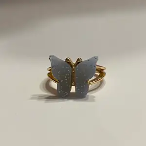 Silverring med gulddetaljer i form av en blå fjäril.