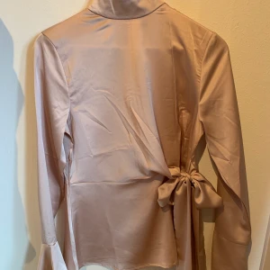 Festtopp boohoo  - Jättefin satinblus/festtopp från boohoo i storlek 34/36. Lite svag rosa/champagne färgad. Band som man kan knyta själv i sidan och lång dragkedja i ryggen. Säljer då den tyvärr inte kommit till användning.