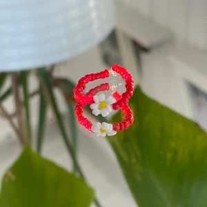 Egentillverkad ring - Röd ring med blomma, egentillverkad! ❣️                   Passar S-M                                                                         Säljer för 15kr + 12kr i frakt. Fraktpriset är det samma oavsett antalet ringar man köper ✨