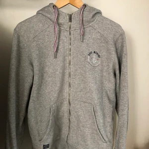 Grå hoodie med dragkedja - Hoodie med dragkedja och muddar. Verkligen tjock och fin kvalité. Sparsamt använd. Sitter lagom löst på mig som är stl. S-M. Möts i Stockholm eller fraktar. Köparen står för frakt.