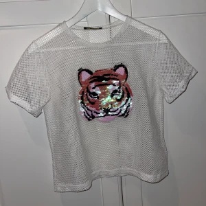 Tröja med tiger  - Säljer min T-shirt som har en tiger på med paljetter som man kan dra ner och upp för att ändra färg, jättefin under en långärmad tröja eller vad som helst, använt 1 gång 