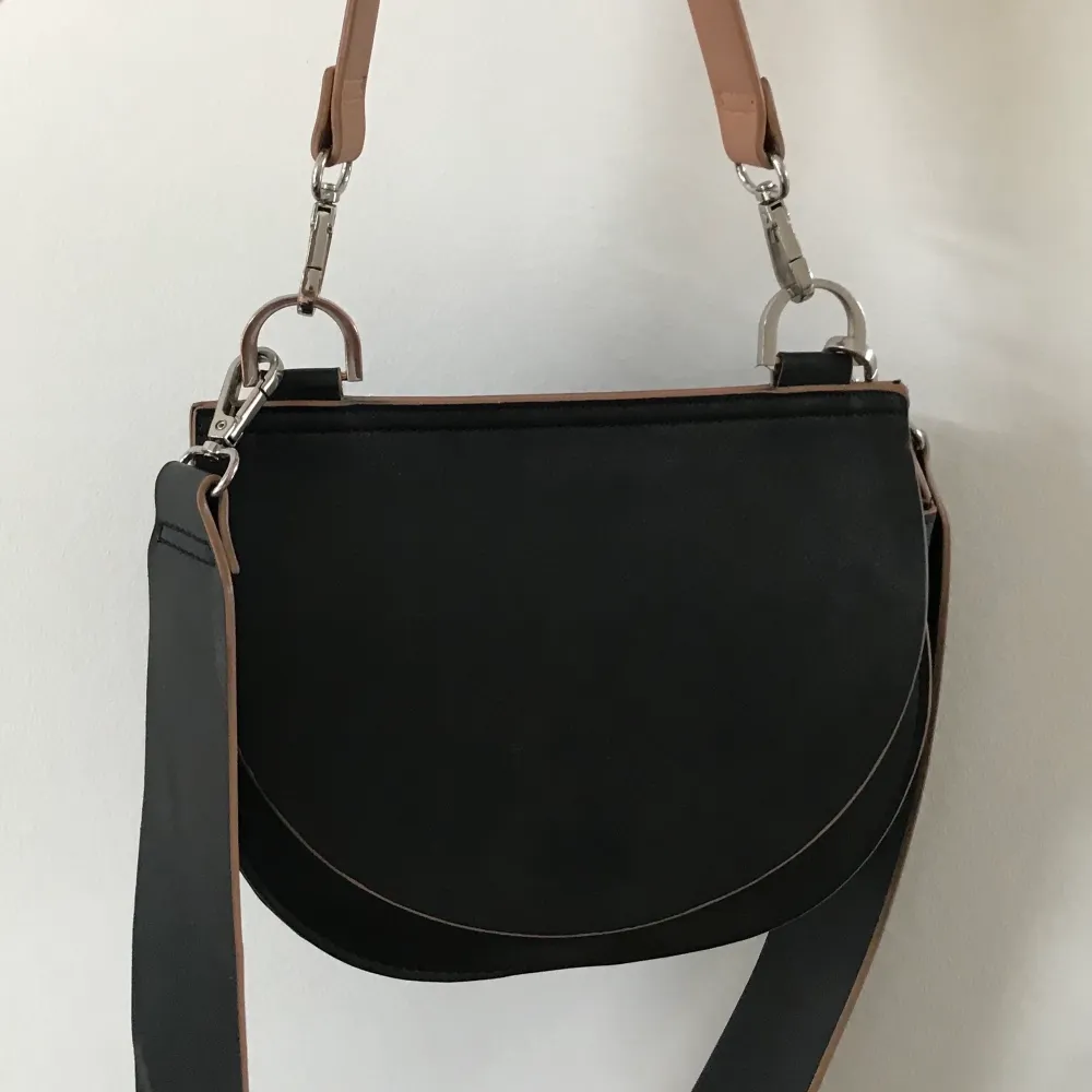 En favorit väska i imitations läder i svart med bruna detaljer . Väskor.