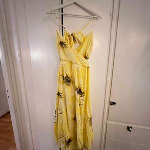 Somrig gul klänning med solrosor. Omlottklänning, rosetten på baksidan knyts hårdare eller lösare för att anpassa storleken. 
