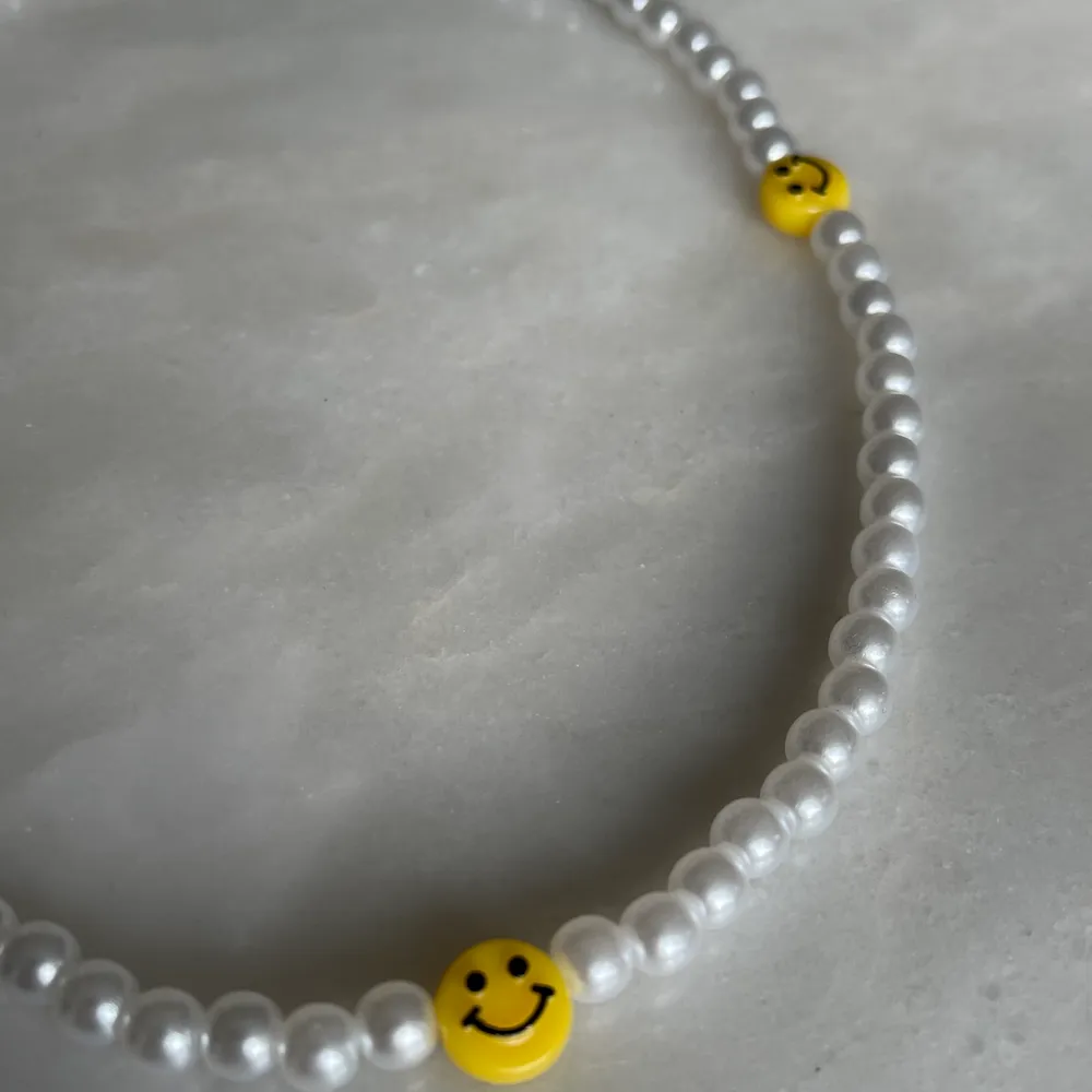 Ett super fint trendigt pärl halsband med tre smileys på.   Storlek 40cm, bandet är även elastiskt samt att det ingår spänne och ringödlor vilket gör att man kan justera halsbandet efter önskad storlek. . Accessoarer.