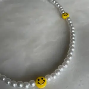 Ett super fint trendigt pärl halsband med tre smileys på.   Storlek 40cm, bandet är även elastiskt samt att det ingår spänne och ringödlor vilket gör att man kan justera halsbandet efter önskad storlek. 