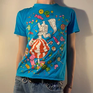 Blå vintage babytee godis all over print - Turkos blå vintage graphic baby tee med ett all over tryck av en astronaut och en massa godis 🍭 Jag är kär i alla detaljer i detta trycket och det bästa är att det är så stort och täcker hela framsidan! Jag älskar också alla olika färger vilket gör det så kul att accessorera med ett par färgglada solglasögon och stora ringar! Sen ett par stora jeans för att bryta av alla färger och ett par funky sneakers!