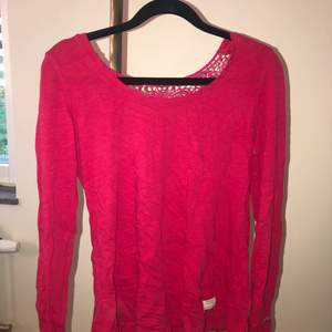 En långärmad tröja med brodyr i ryggen baktill . Använd 1 gång . Mörk rosa i färgen .