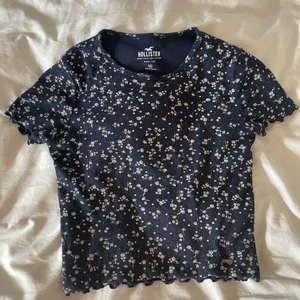 Hollister topp  - Jättefin mörkblå ribbad topp från Hollister i storlek xs. Skulle säga att den mer är storlek S och är väldigt stretchig så skulle därför passa S/M hur bra som helst. Den har detaljer av vita blommor. Säljer eftersom den tyvärr aldirg kommer till användning. Nypris ca. 200kr på Hollisters hemsida.