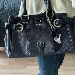 Svart vintage väska från Sisley - Supersnygg och trendig vintage väska från Sisley. Rymmer mycket och super fina silver detaljer! Dock ganska använd vilket resultat i defekter på handtaget. Köpt för 600kr. Väskan har supercoola detaljer över hela väskan med märkes logga. Fråga för fler bilder! (Kunden står för frakten)